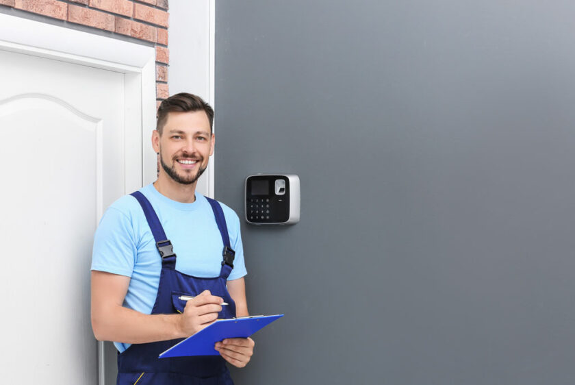 Male technician with clipboard near installed alarm system indoors